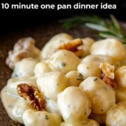 Pin Image: Gnocchi in gorgonzola sauce with walnuts on a brown plate and a rosemary sprig with text overlaid