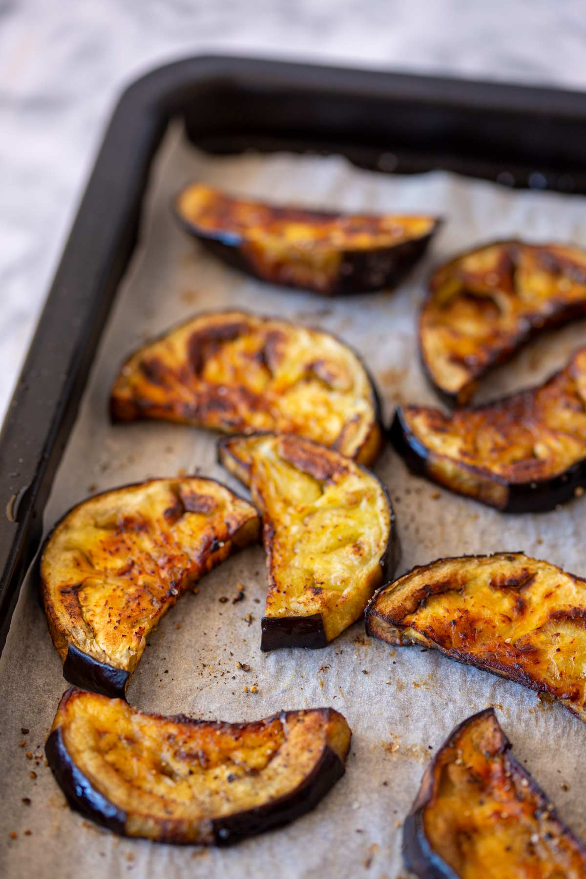 roasted eggplant slices on a baking sheet lined with parchment paper. The slices are golden brown with caramelized edges