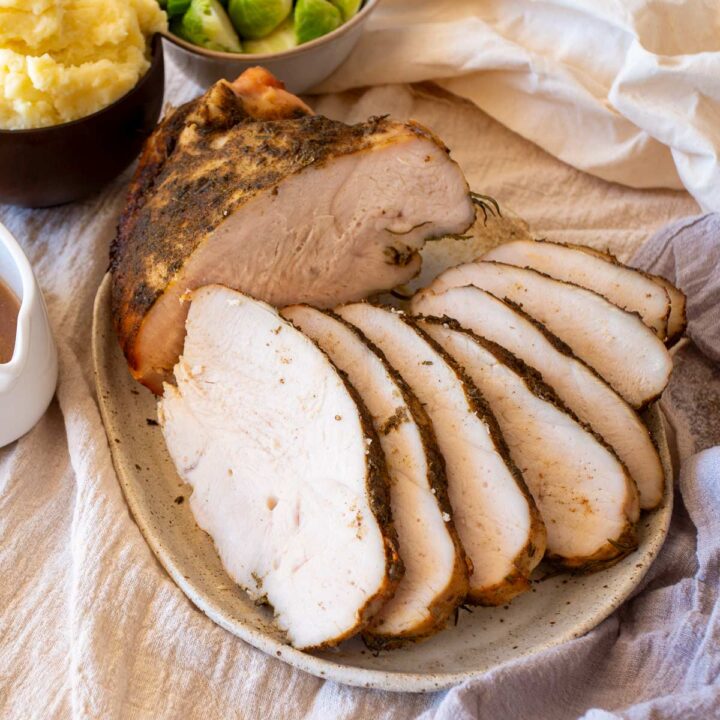 Carved slices of turkey breast arranged on a rustic plate with sides in the background