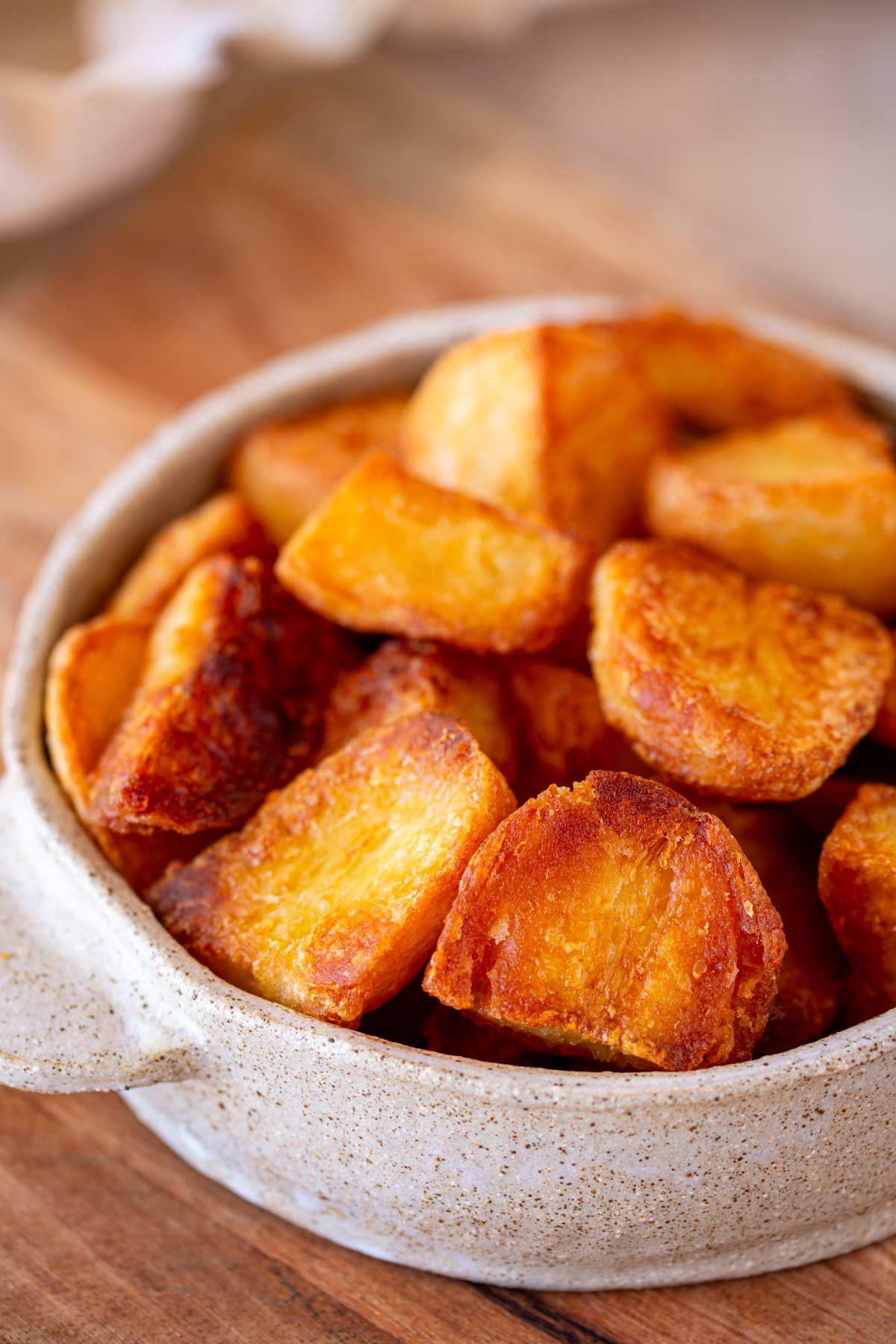 A rustic stone bowl filled with golden roast potatoes, sitting on a wooden surface for a cozy, homey feel