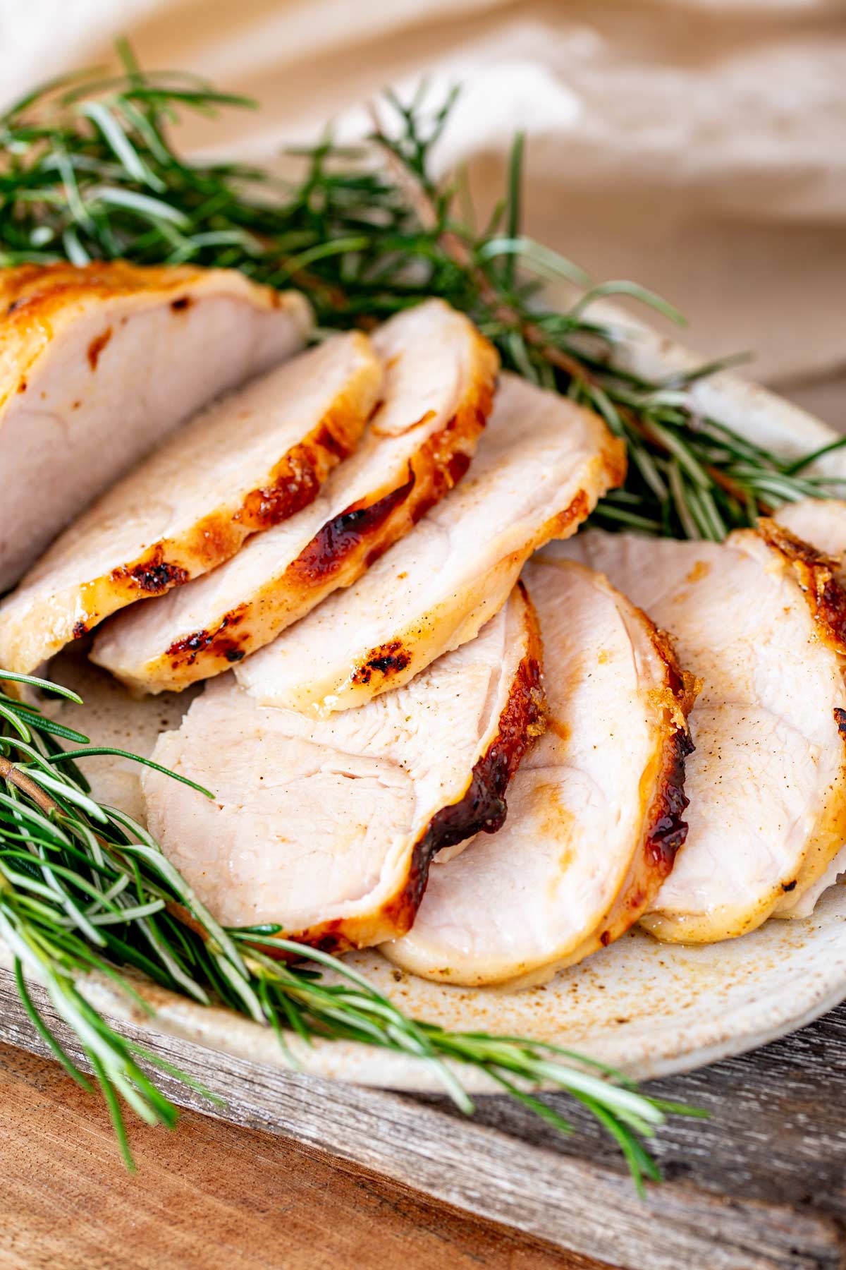 Close-up view of juicy turkey breast slices resting on a ceramic plate, accented by fresh rosemary.