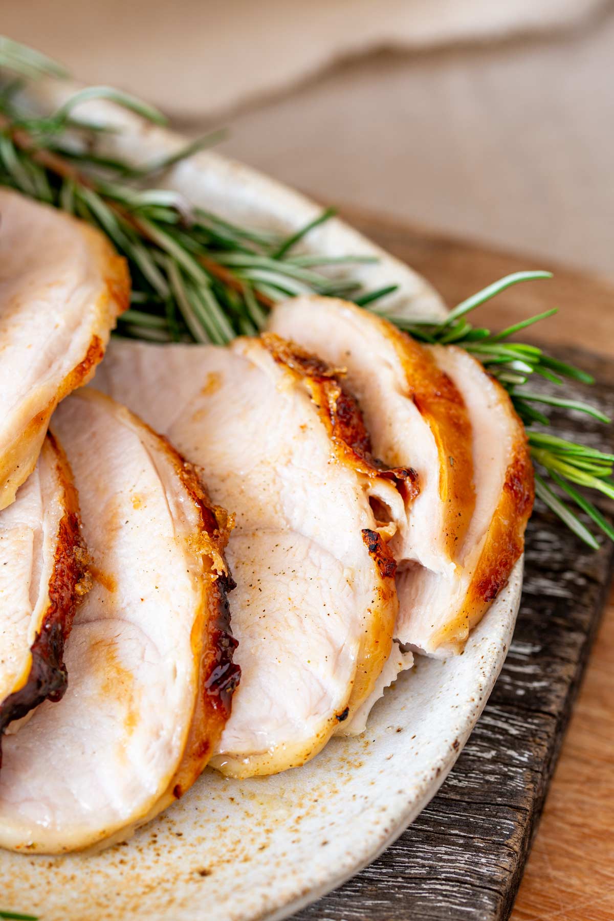 Close-up of turkey slices, highlighting the texture and placement on a simple ceramic plate with rosemary.