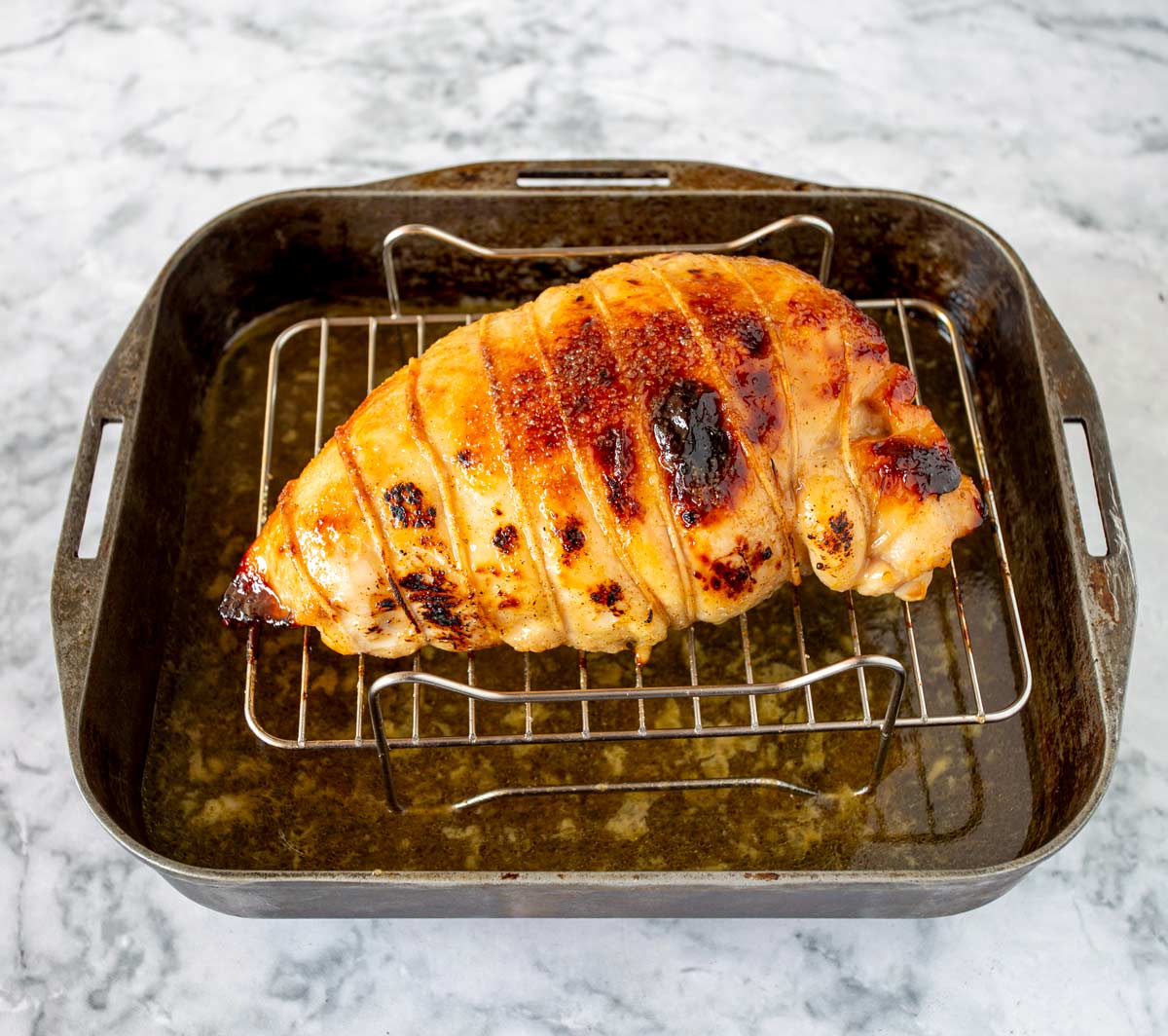 Golden roasted turkey breast with a crispy surface, tied with string, sitting in a baking pan filled with drippings.