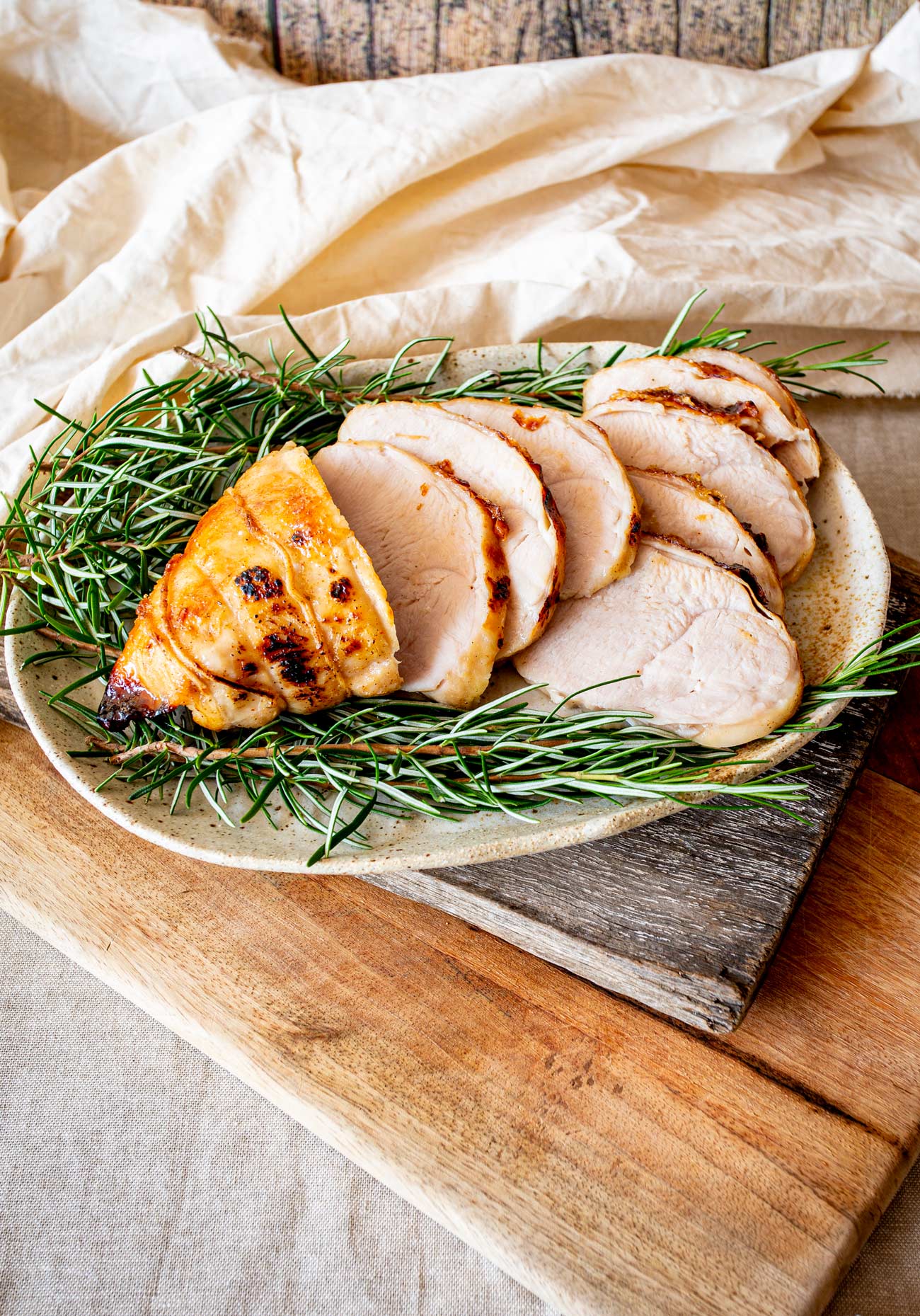 Slices of turkey breast arranged on a neutral plate with rosemary sprigs on the sides, resting on a textured wooden backdrop.