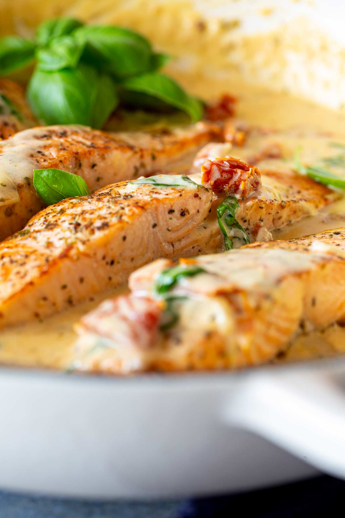 Close-up of pan-seared salmon fillets in a creamy basil sauce with fresh basil leaves in the background, highlighting the herbs and smooth sauce texture.