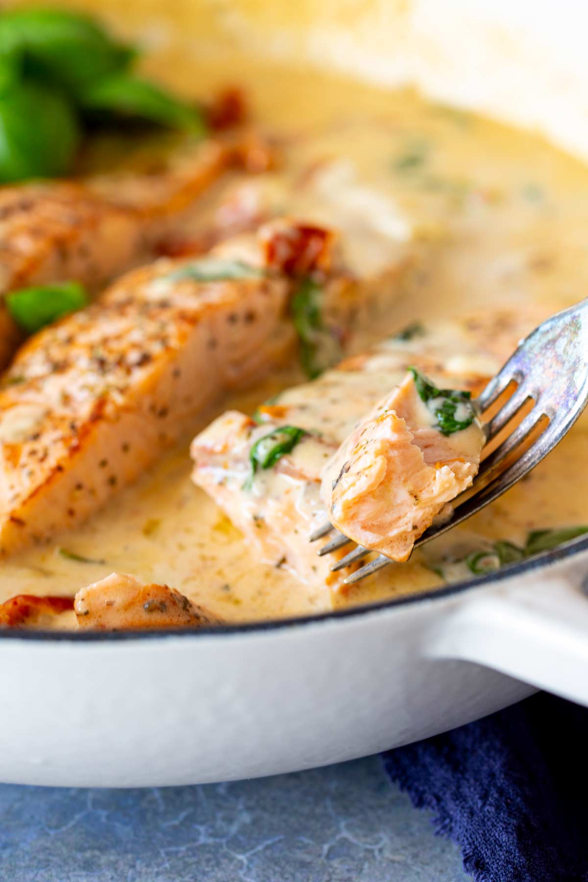 Close-up of a fork holding a piece of salmon, showing its tender, flaky texture with creamy sauce and basil leaves in the background, highlighting the rich and comforting flavors.