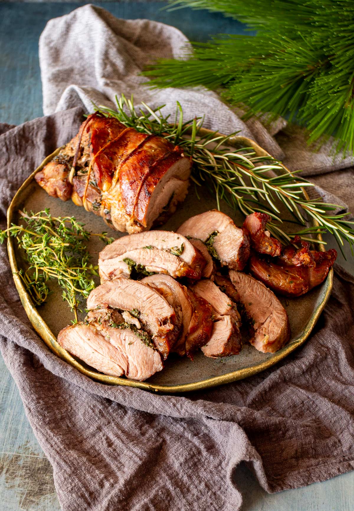 Rolled turkey thigh slices arranged on a plate, revealing the herbs inside, with a grey cloth and greenery in the background.