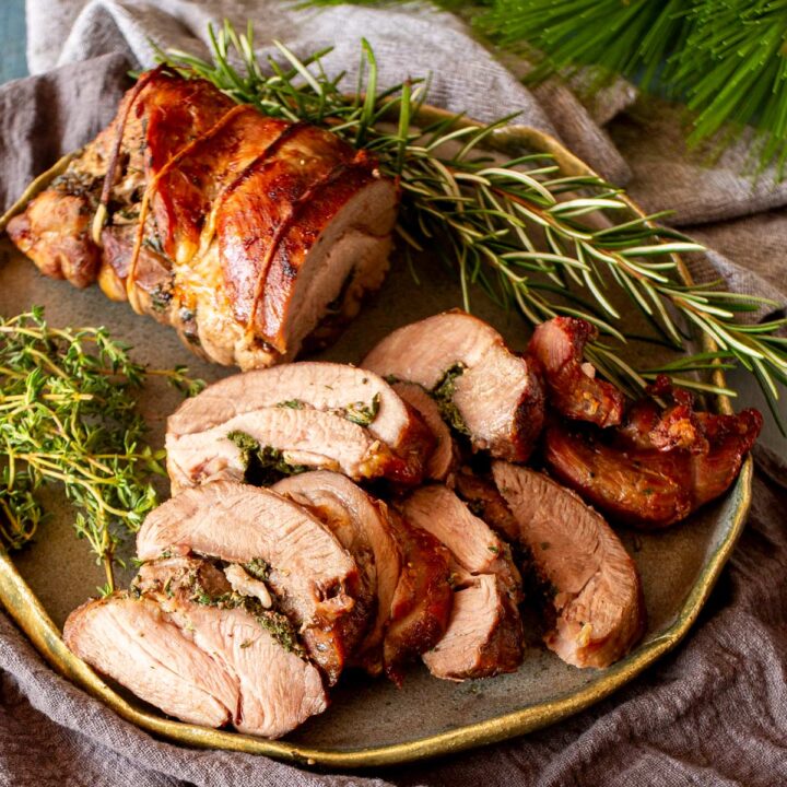 A sliced rolled turkey thigh stuffed with fresh herbs and tied with twine, served on a plate with sprigs of rosemary and thyme.