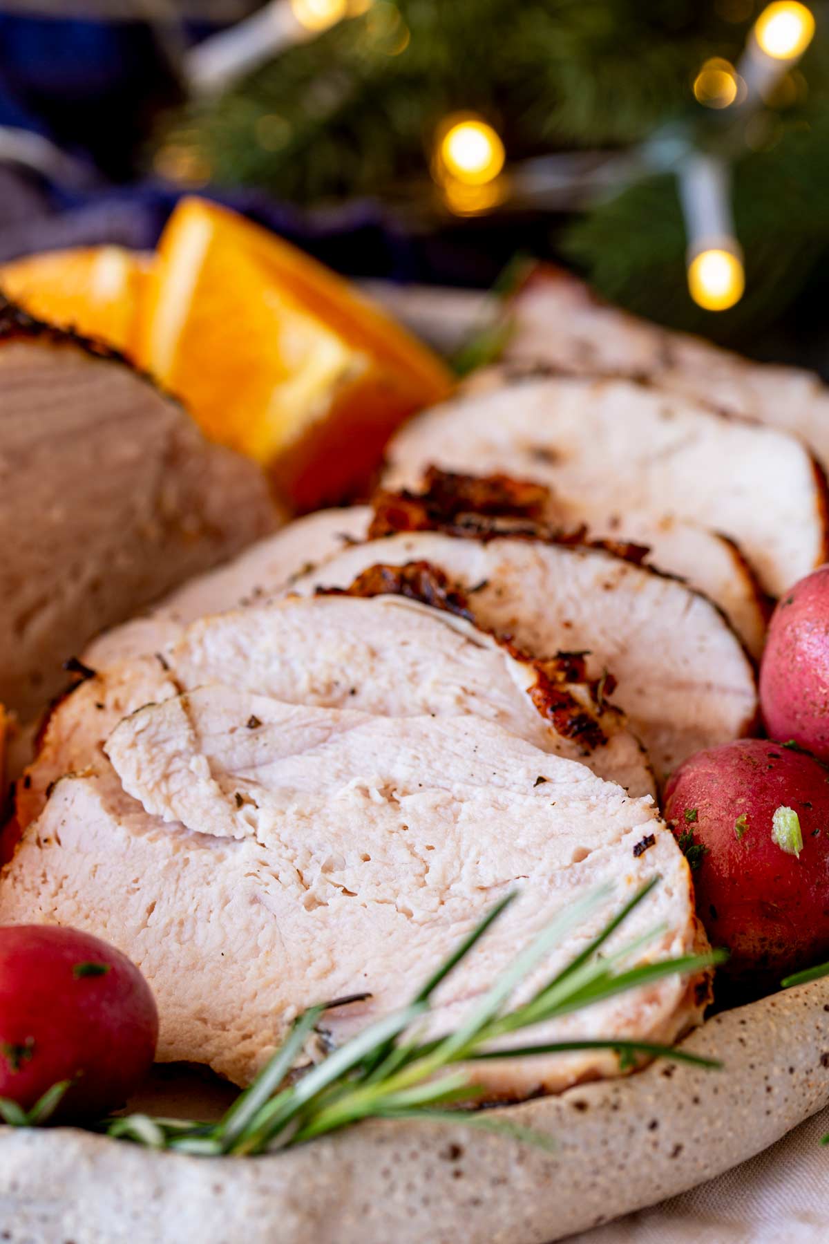 A focus on tender turkey slices, garnished with rosemary and citrus, while blurred holiday lights create a warm ambiance in the background.