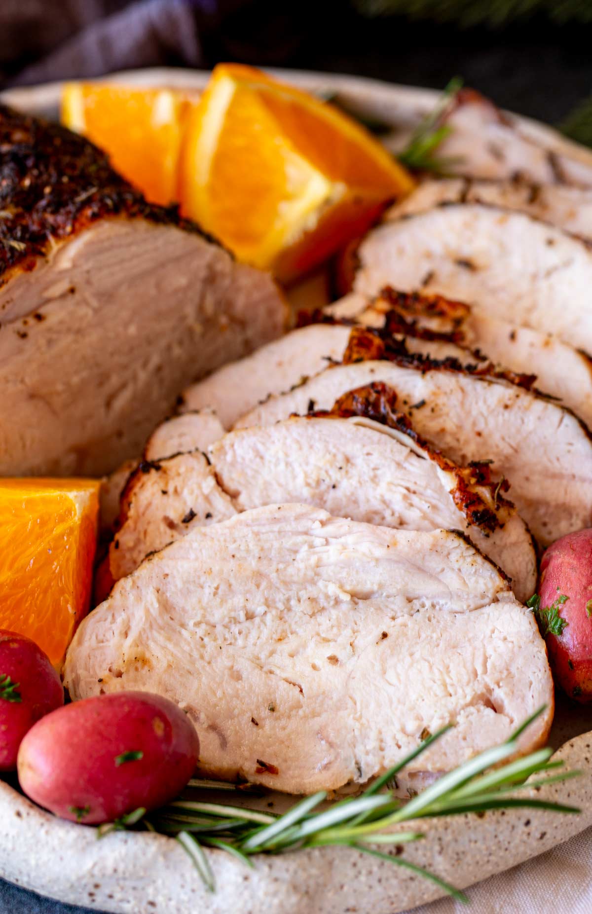 A zoomed-in angle of turkey slices arranged in layers, with visible herbs on the crust and colorful garnishes of citrus and potatoes.