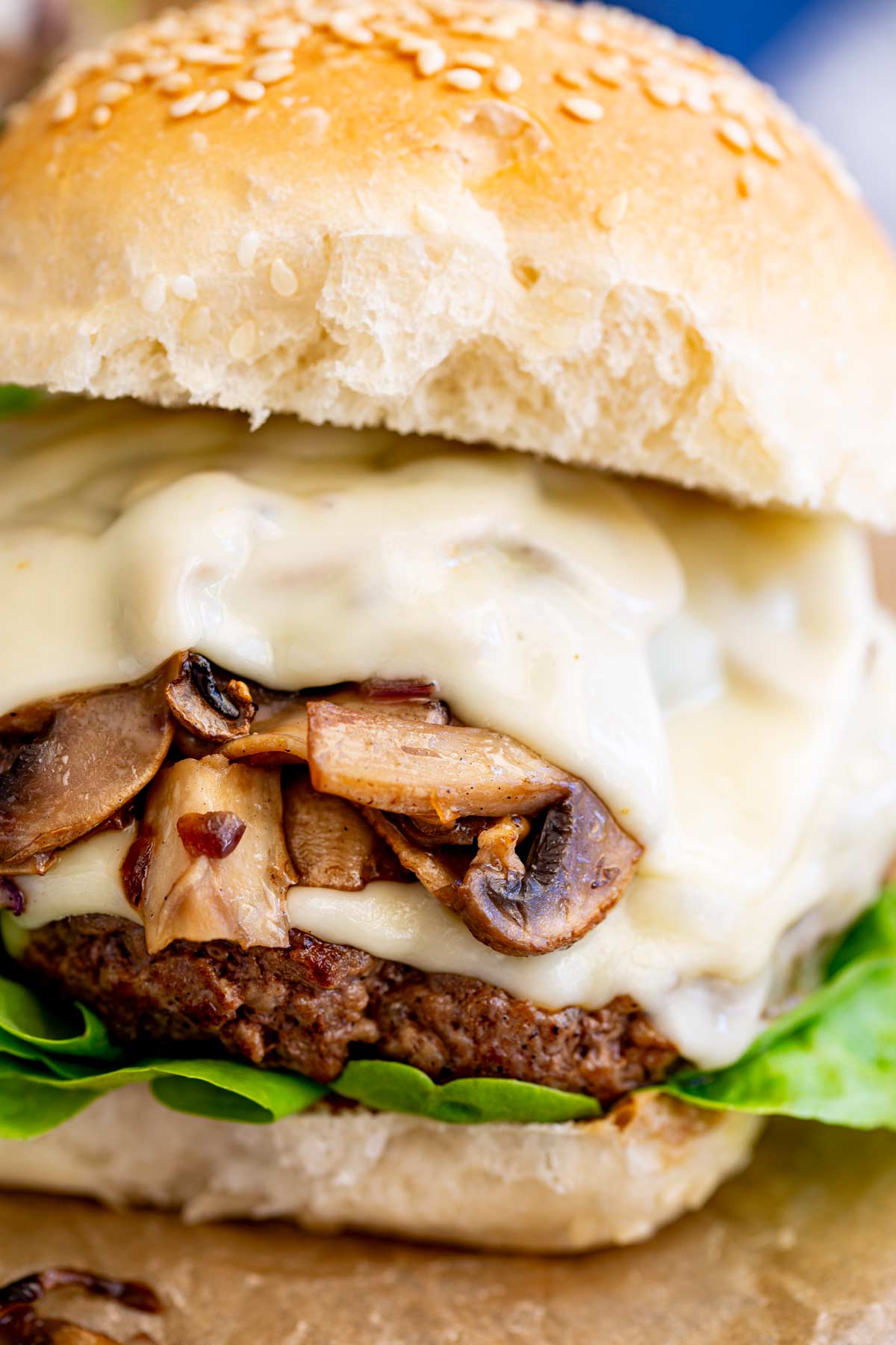Close-up of a stacked beef burger with Swiss cheese, sautéed mushrooms, and a toasted bun