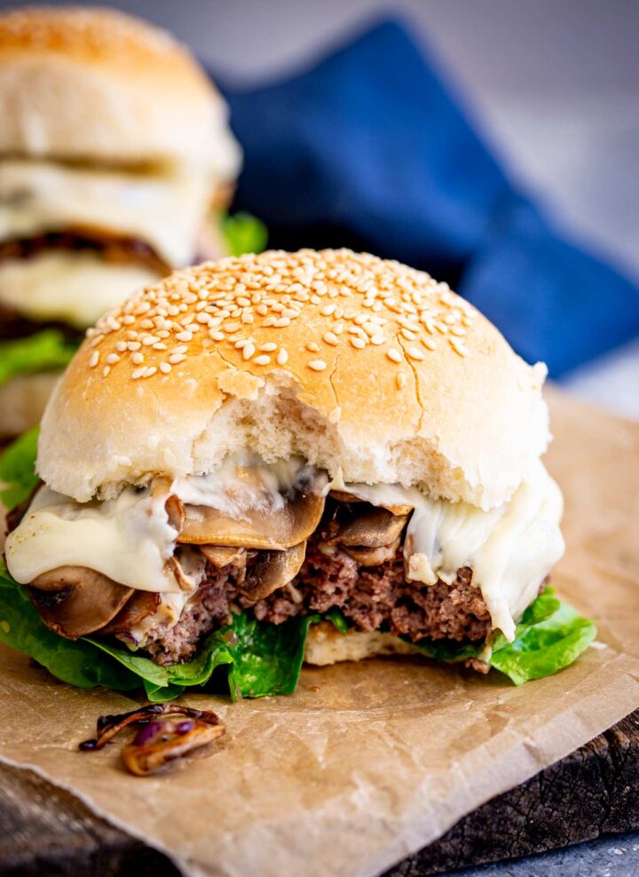 A hearty, cheese-topped burger with mushrooms, with a lightly toasted sesame bun, presented with a bite taken out of it