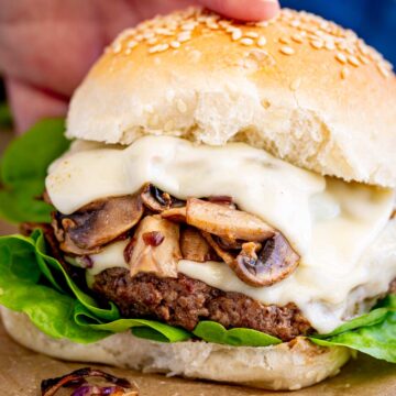 Close-up of a beef burger stacked with melted cheese and sautéed mushrooms, showing off the textures of the patty and bun