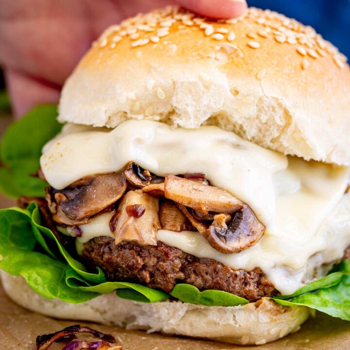 Close-up of a beef burger stacked with melted cheese and sautéed mushrooms, showing off the textures of the patty and bun