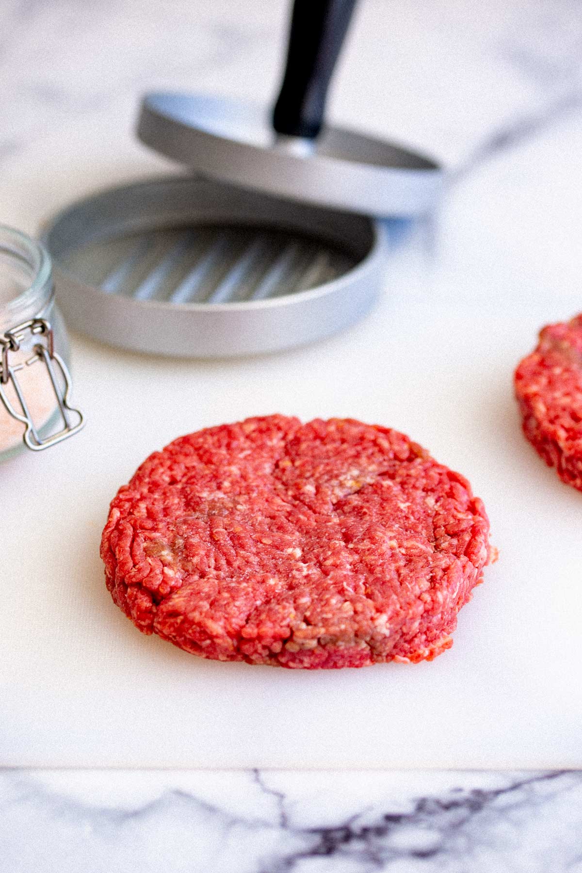 a raw beef burger on a plastic board with a burger press in the background