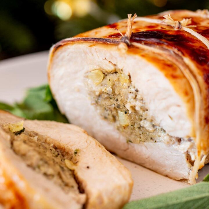 A close-up view of a rolled turkey breast stuffed with sage and onion stuffing, tied with twine and roasted to a golden brown.