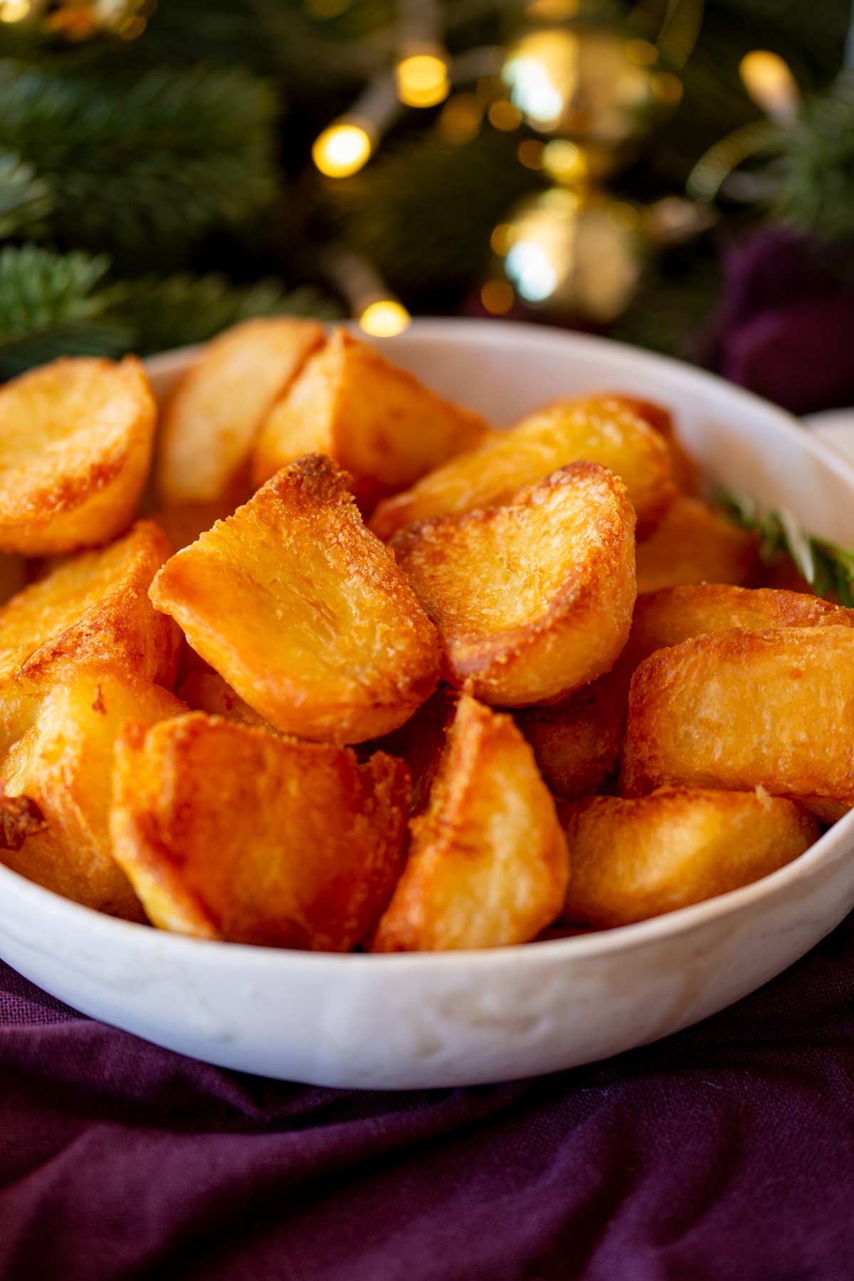 A white serving dish filled with golden roasted potatoes with Christmas decoration behind