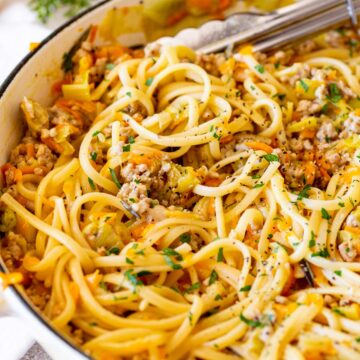 A close-up of linguine in a white cast iron pan, showing pasta coated in a leek, carrot and pork sauce