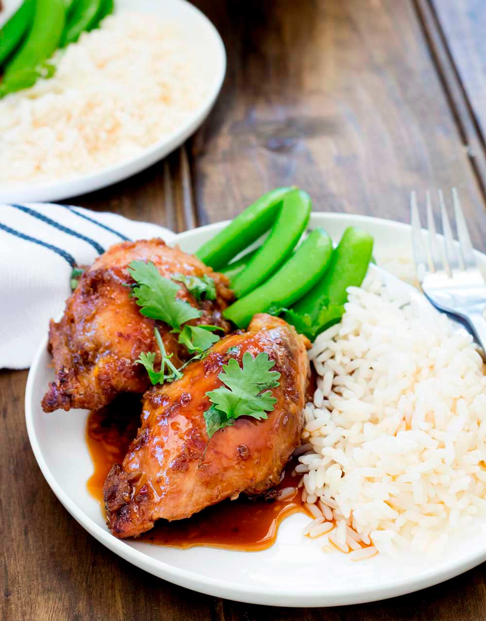 two pieces of chicken with rice and sugar snap peas on a white plate on a wooden table