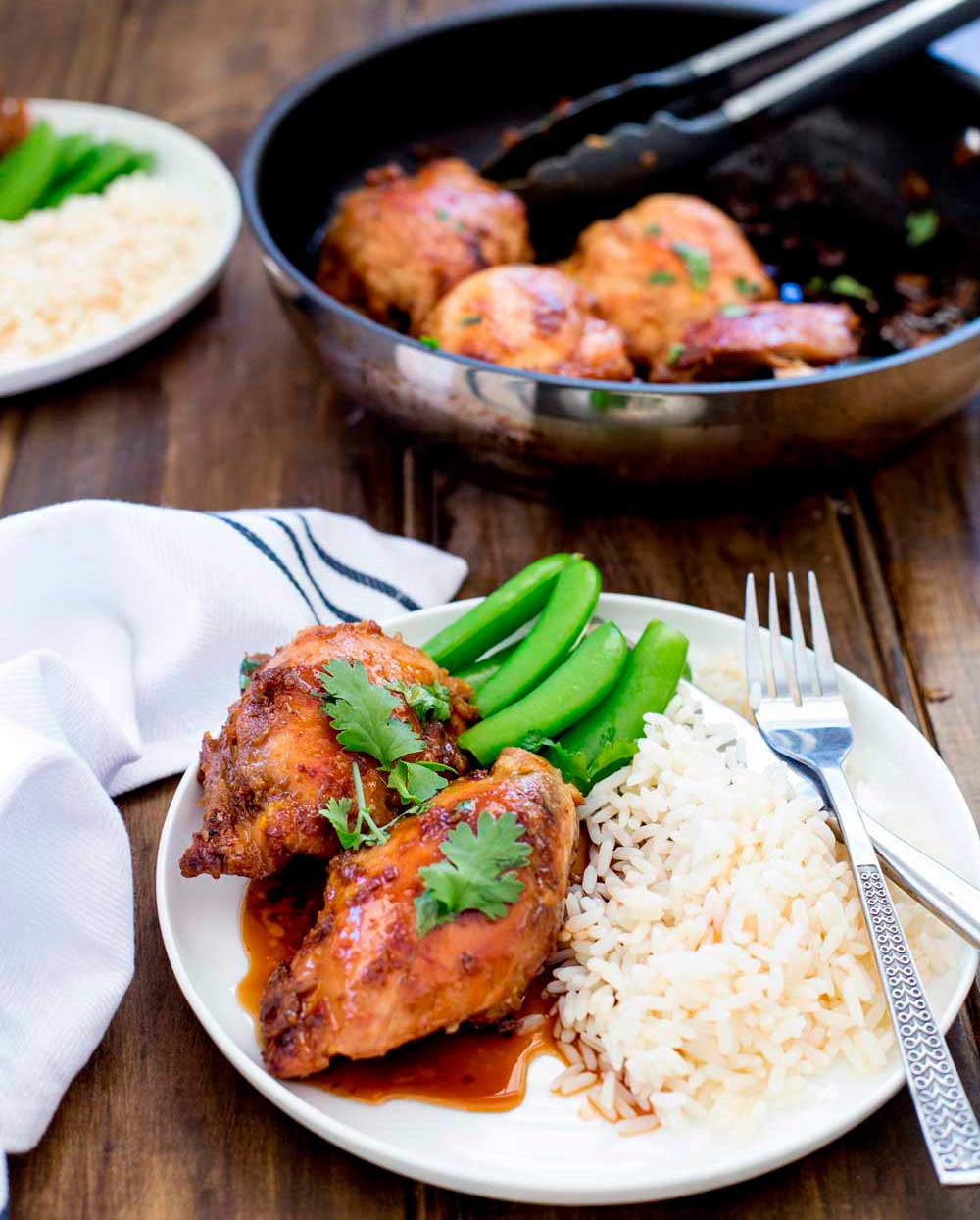 a plate of chicken and rice with a pan of chicken in the background