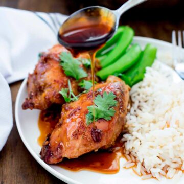 close up of a spoon drizzling sticky sauce over coconut chicken thighs