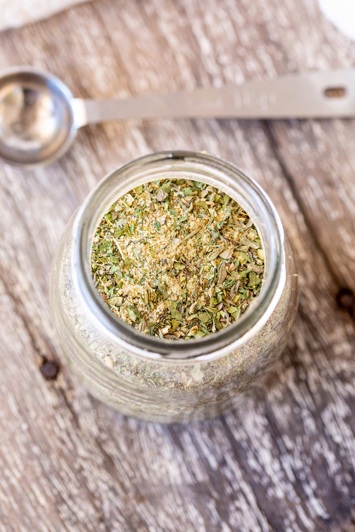 Overhead on a small glass jar filled with a homemade seasoning blend, showing a mix of dried herbs and spices.