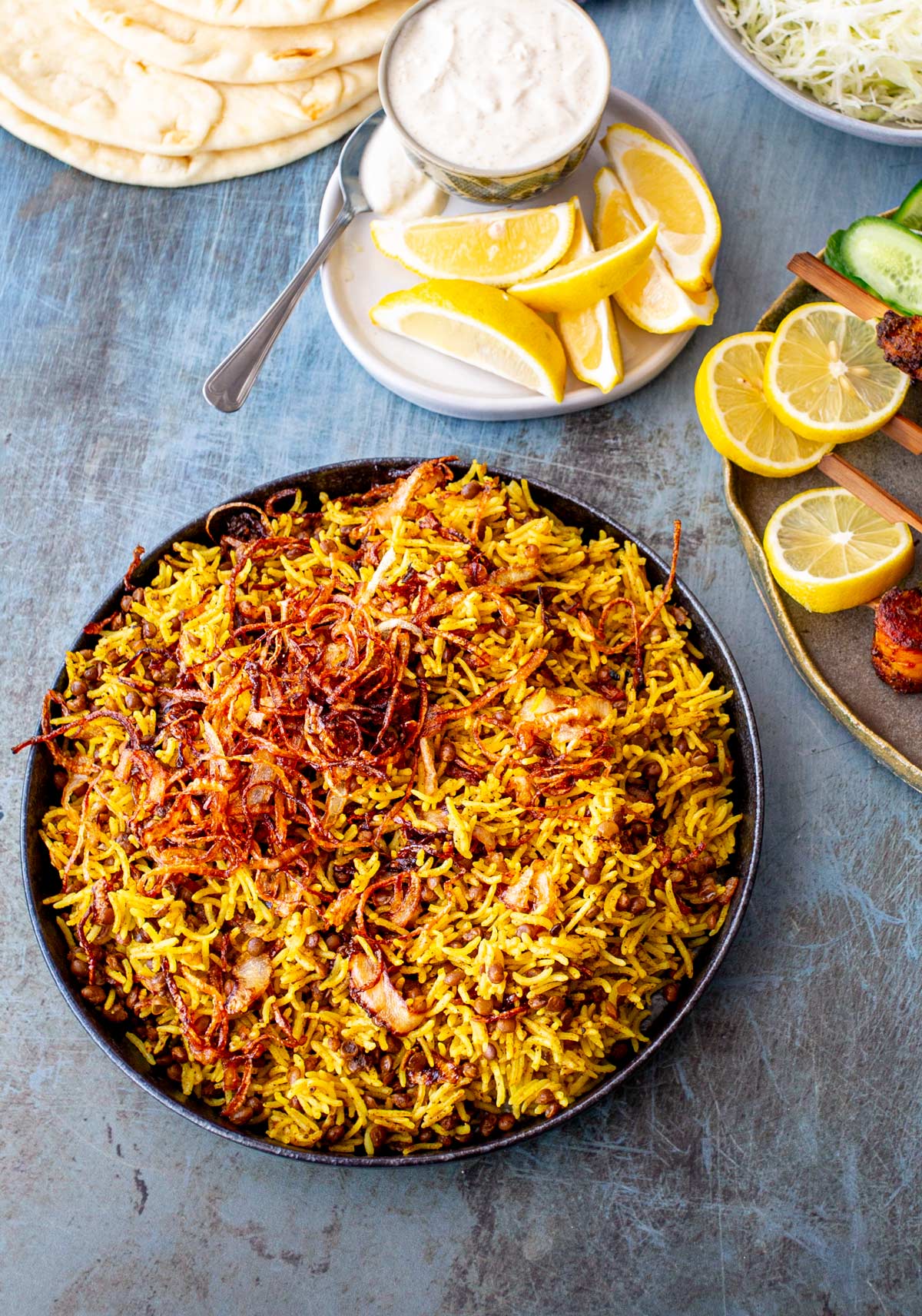 A top-down view of Mejadra, served with chicken shawarma skewers, yogurt, and flatbread.