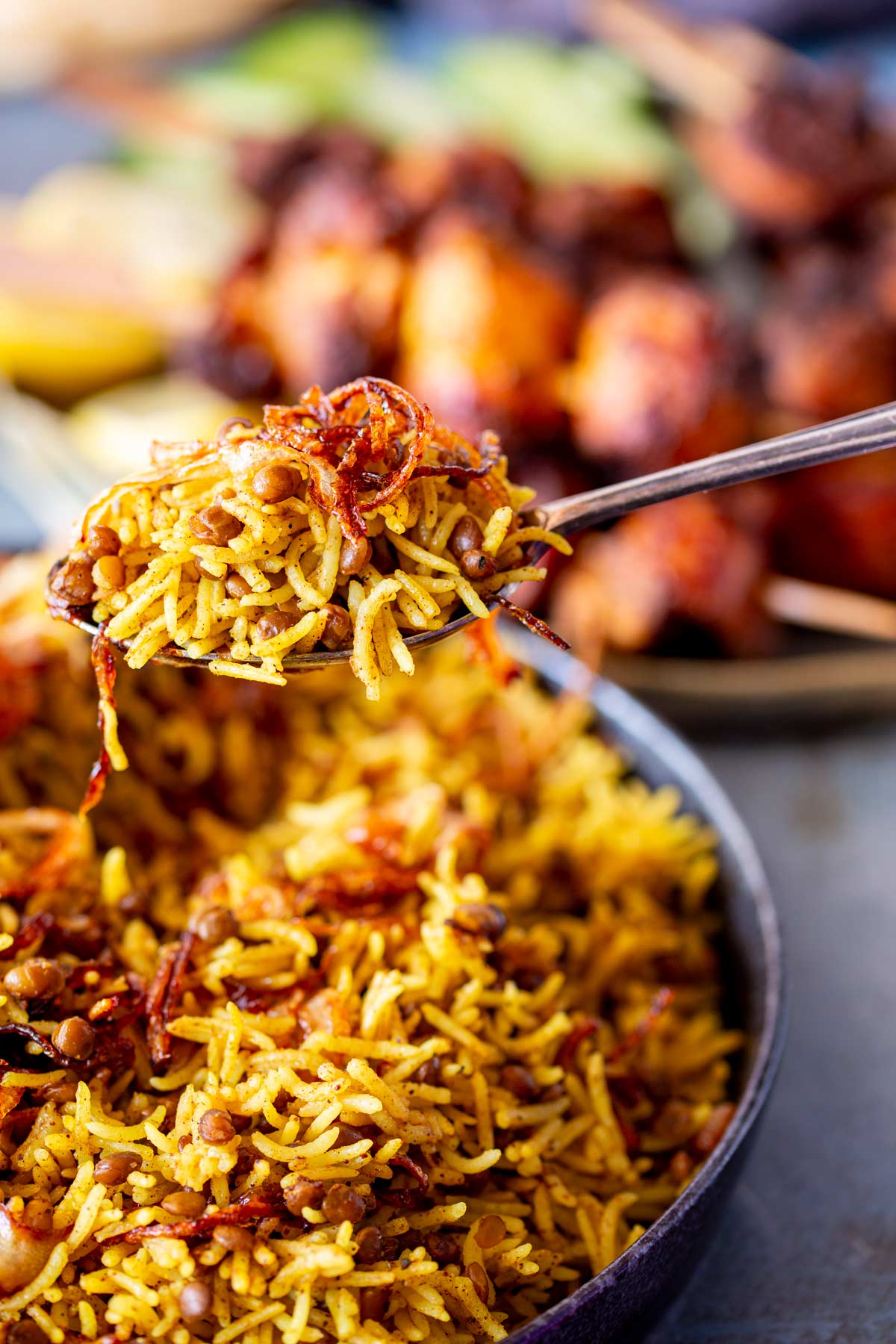 A close-up of Mejadra on a spoon, showing the fluffy spiced rice, lentils, and crispy fried onions.