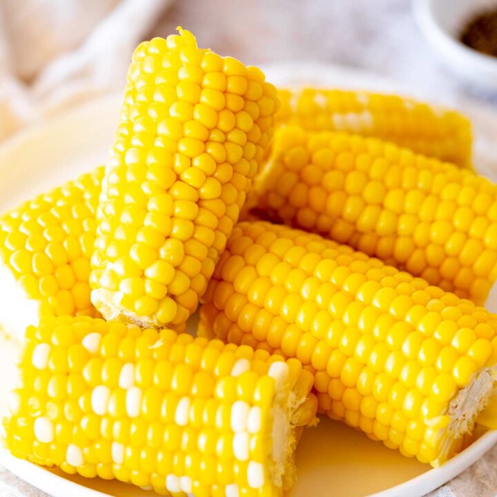 a white plate piled with cooked corn on the cobs With no husk or silks