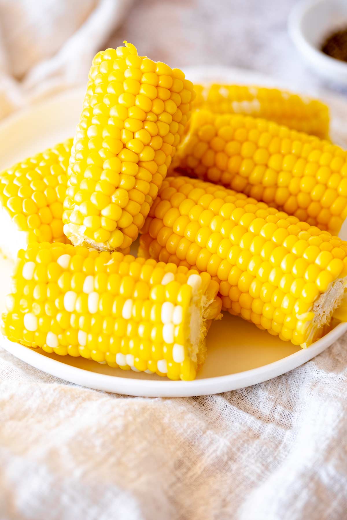 corn on the cob cut in half on a white plate with a linen table cloth beneath