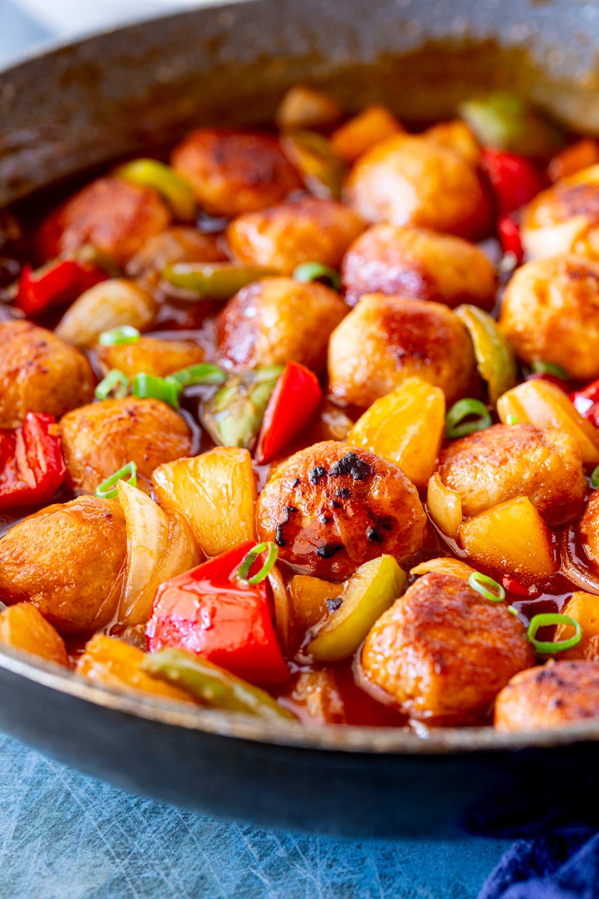 A close-up of a skillet packed with chicken meatballs, covered in a rich, tangy sauce with chunks of pineapple and red and green bell peppers.