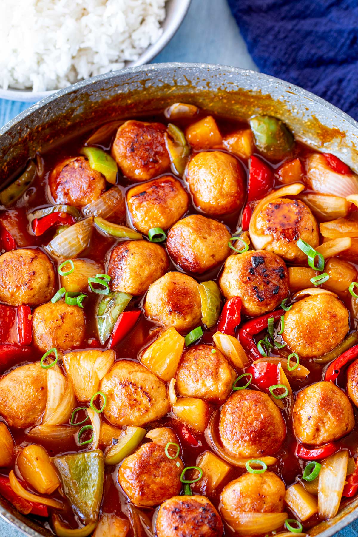 A pan of meatballs in a red sauce with vegetables and pineapple