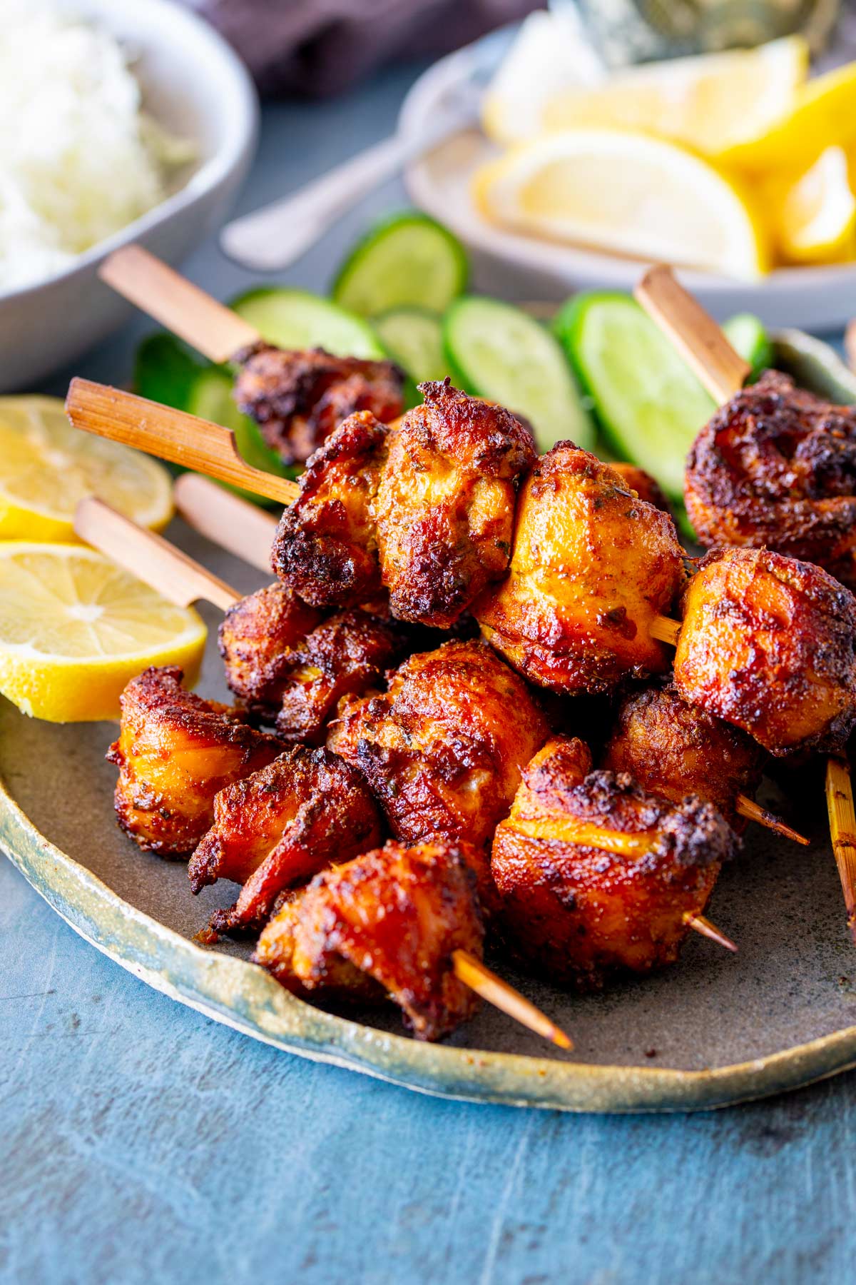 A plate of golden charred chicken skewers accompanied by cucumber slices and bright lemon wedges.