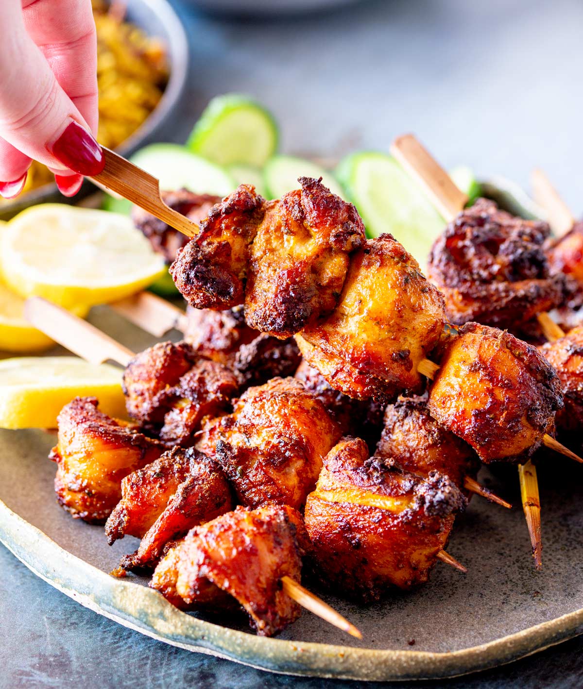 A hand lifting a chicken skewer, showing the juicy, charred meat.