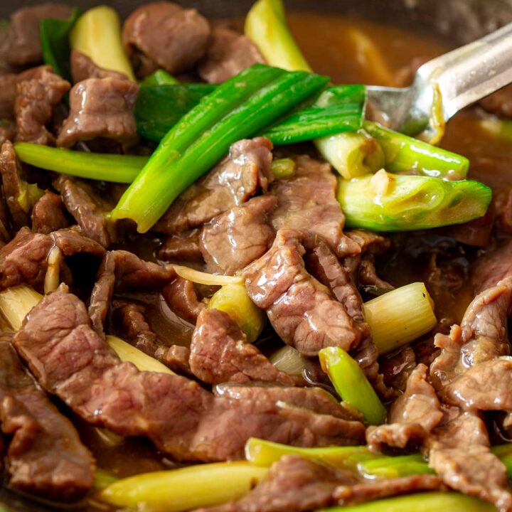 A detailed close-up capturing the glossy texture of tenderised beef strips coated in a Chinese brown sauce, tossed with bright green spring onions.