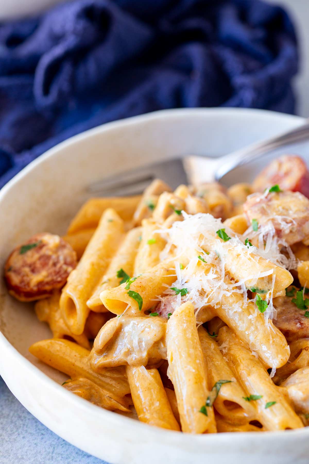 A portion of creamy chicken and chorizo pasta served in a shallow dish, with a crumpled blue napkin in the background