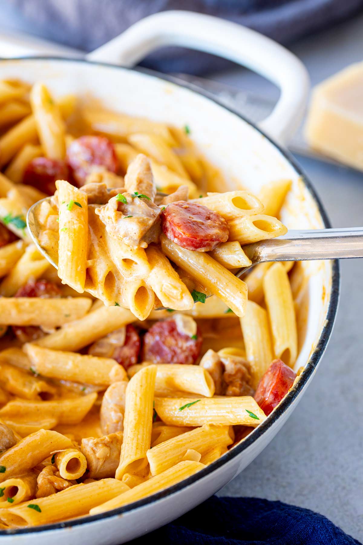 A spoon scooping creamy chicken and chorizo pasta from pan.