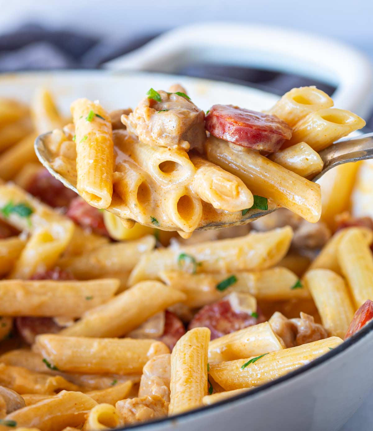 close up on a serving spoon scooping creamy penne from a pan