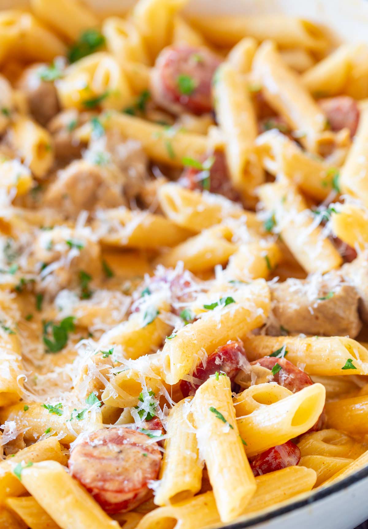 A close-up showing tender chicken thighs and vibrant chorizo rounds coated in creamy sauce with penne pasta, sprinkled with parmesan
