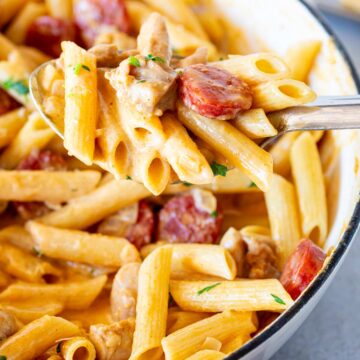 close up on a serving spoon scooping up pasta, chicken and chorizo from a pan
