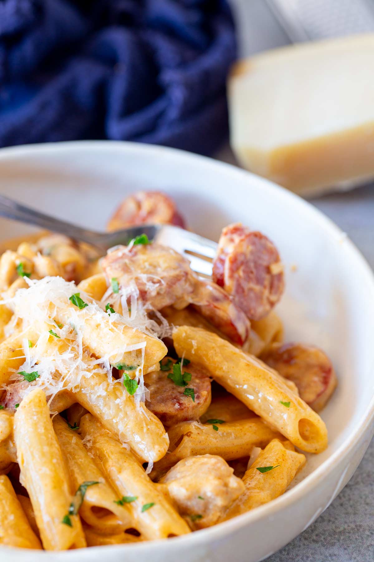 a fork stabbing a piece of chorizo from a bowl of creamy pasta with a blue napkin in the background