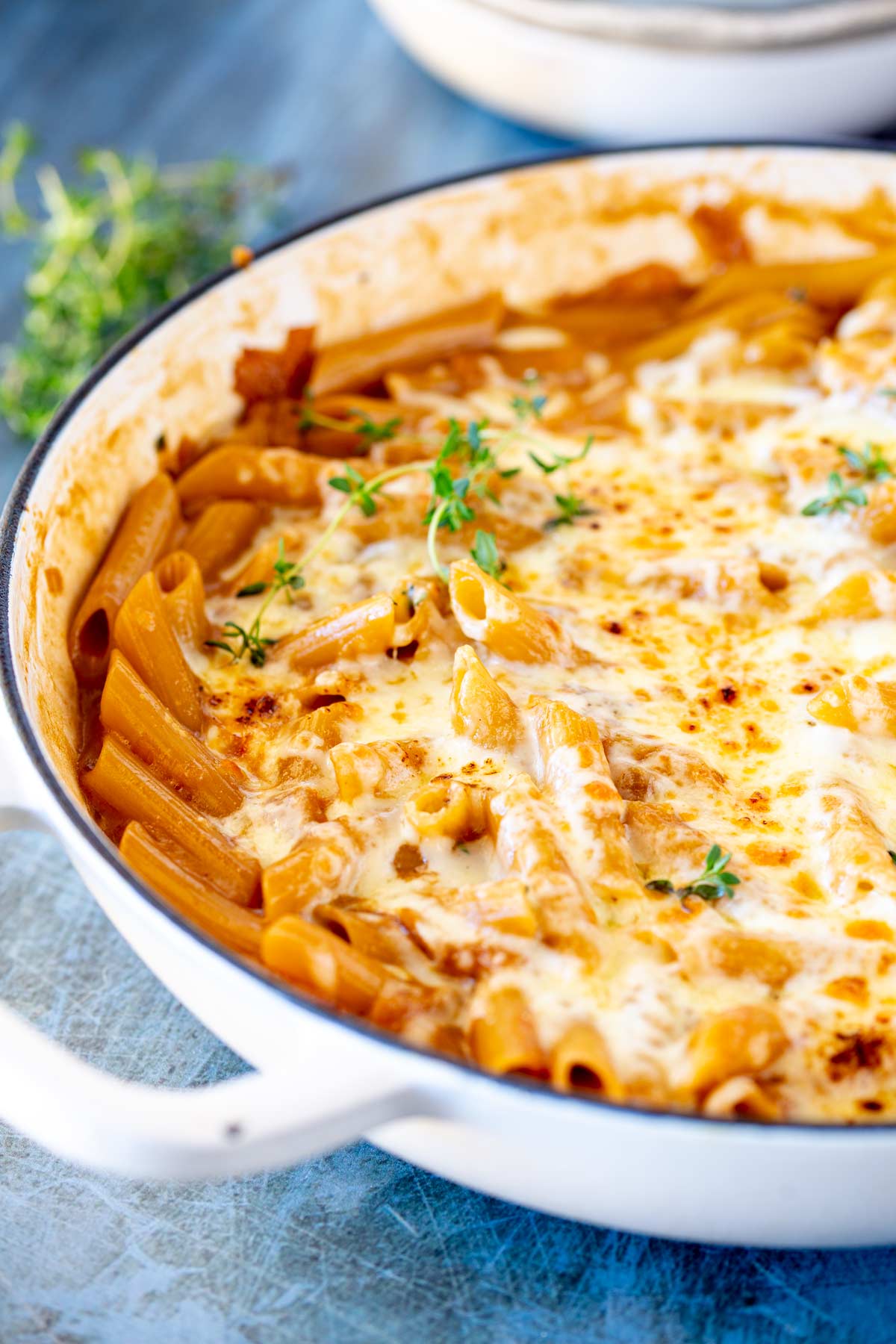 creamy skillet filled with cheesy onion pasta garnished with fresh thyme on a blue scratched surface
