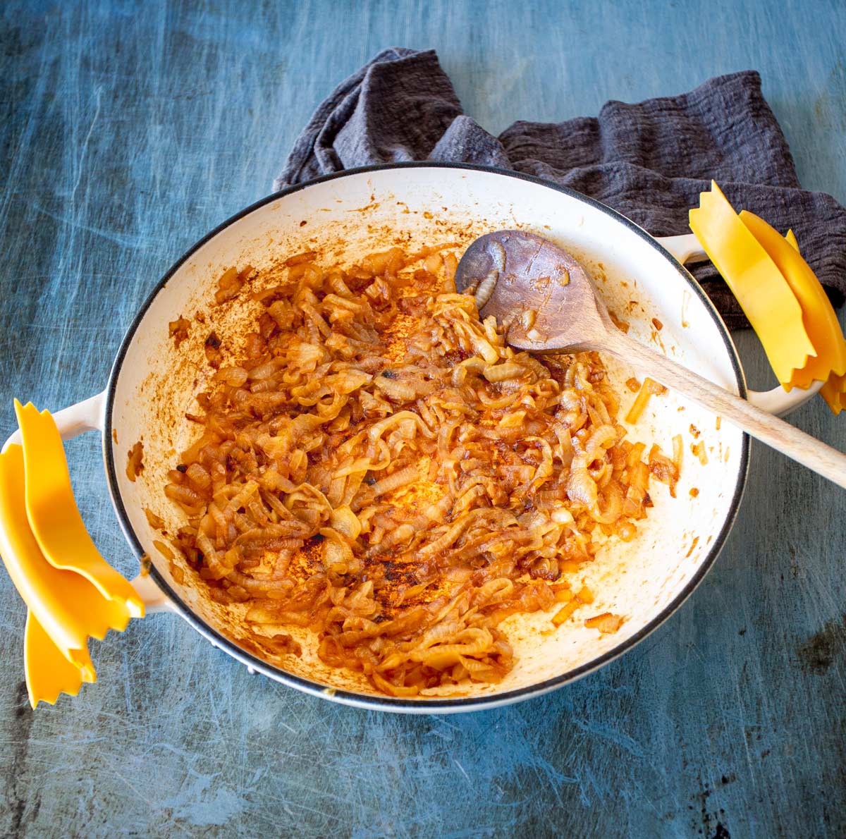 Overhead shot of a white handled skillet with caramelised onions on a scratched blue-toned metal surface