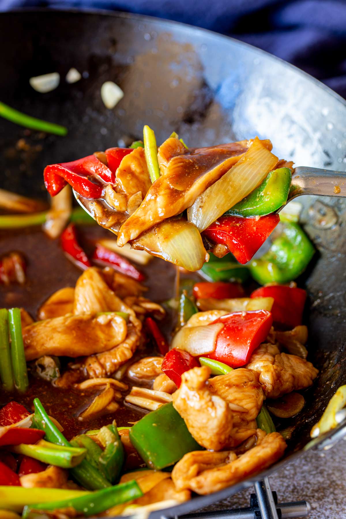 a silver spoon scooping chicken and peppers from a wok with a sticky brown sauce