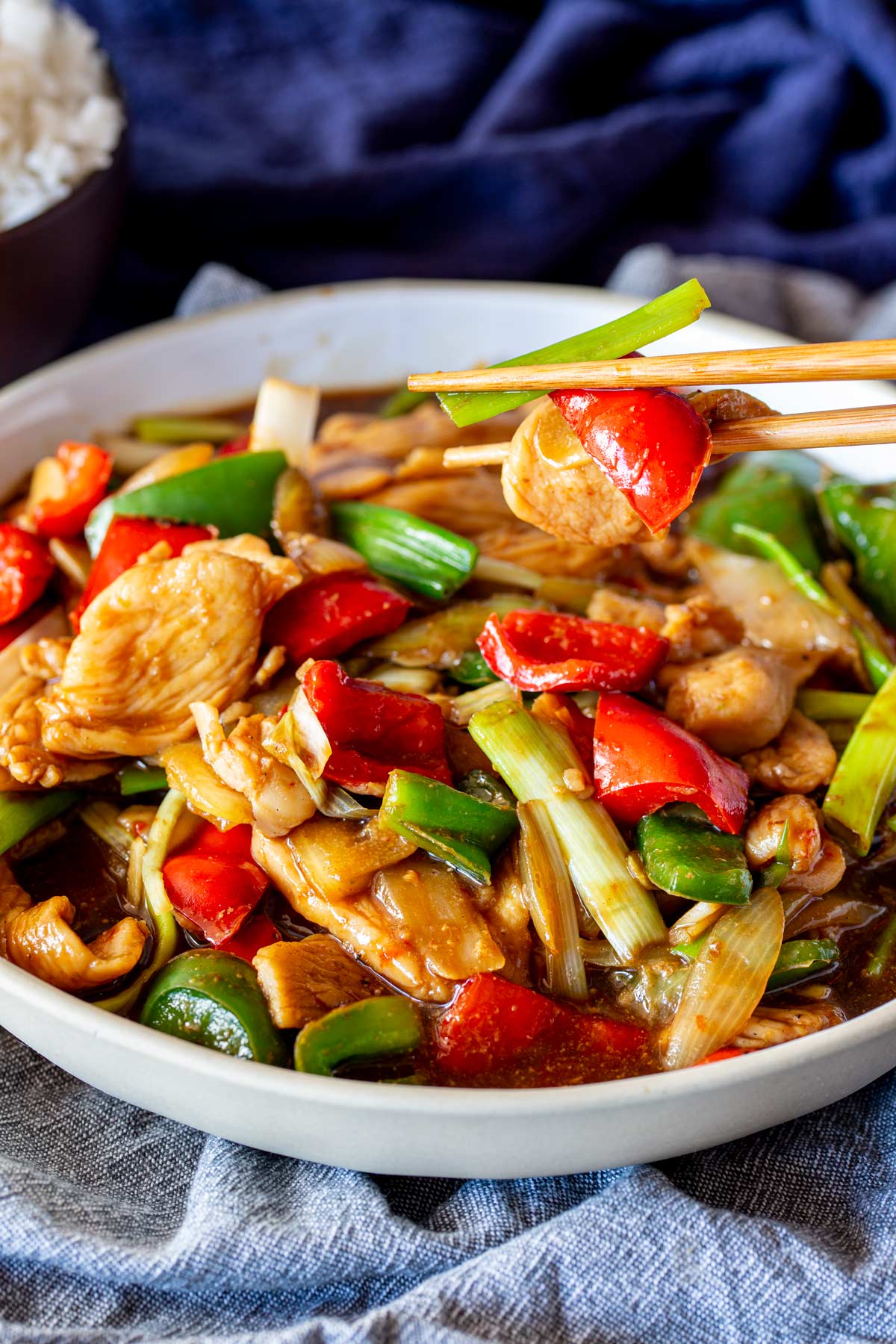 A strip of chicken being lifted by chopsticks from a bowl of colorful stir-fry