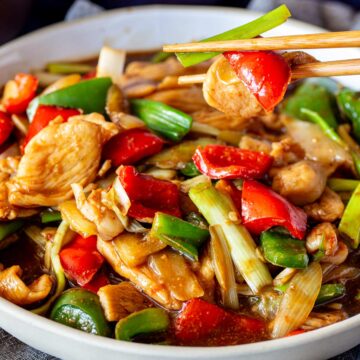 a close up of chopsticks lifting some chicken and peppers from a dish of stir fry