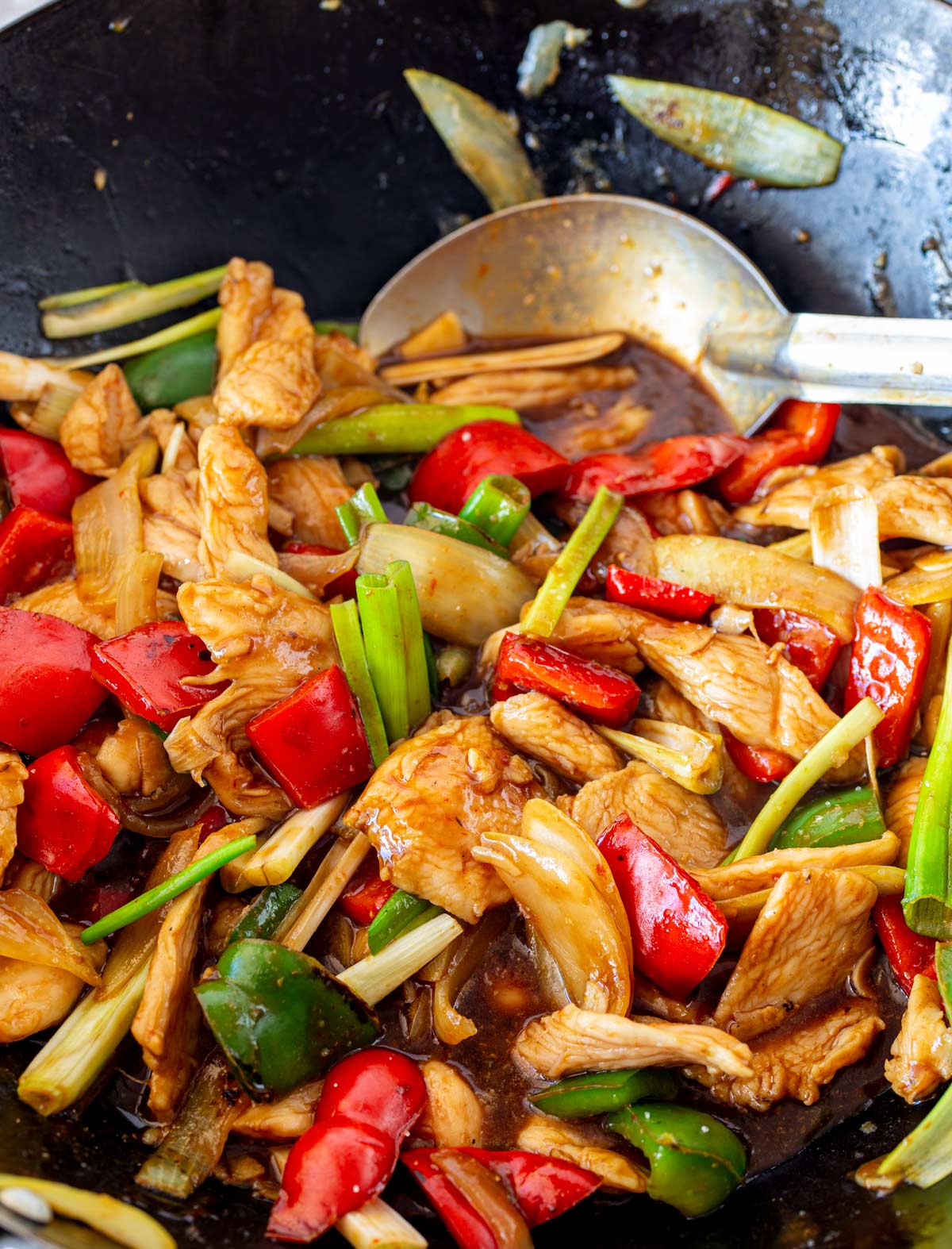 Wok filled with chicken, spring onions, and peppers, with a metal serving spoon resting inside