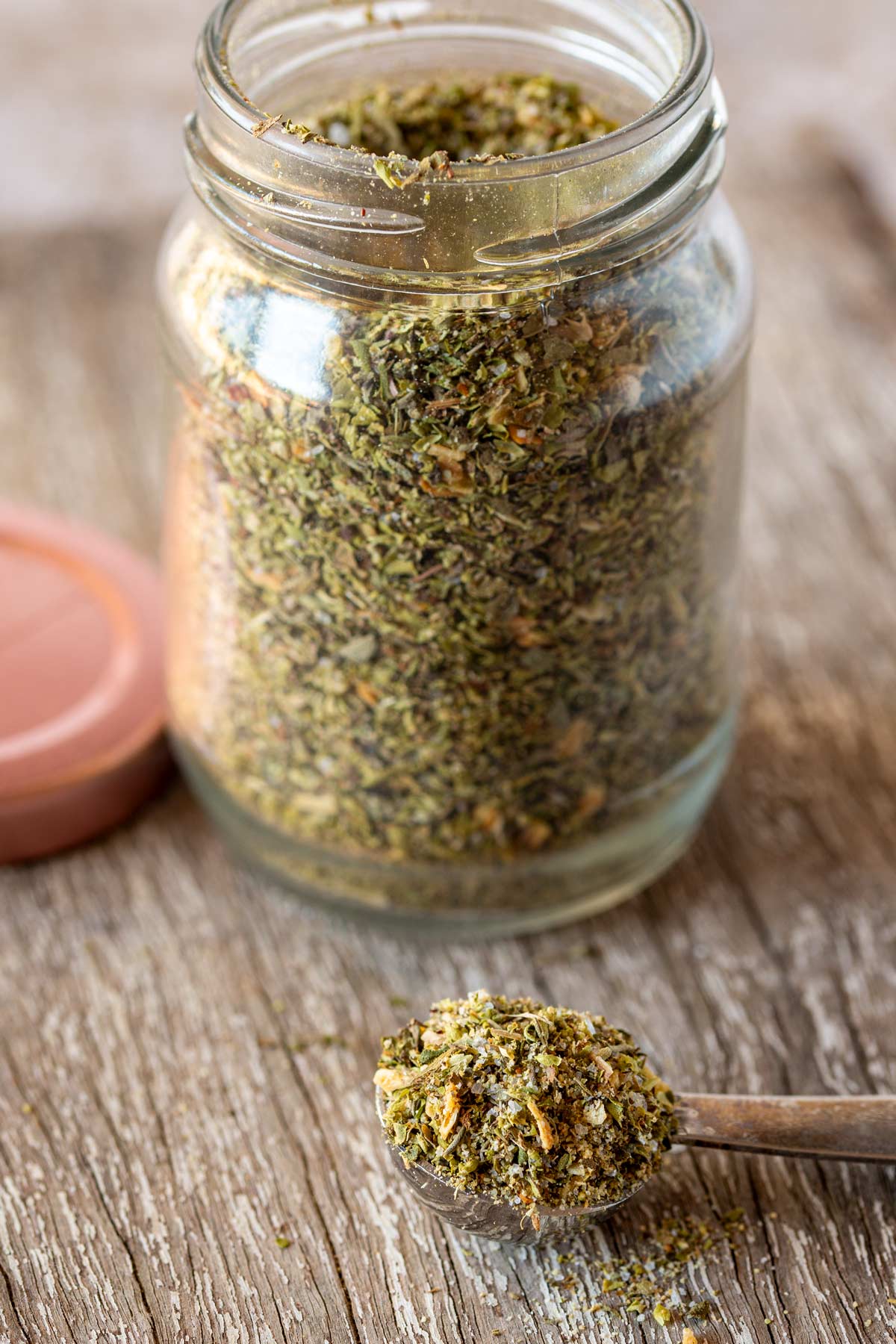 Dried herb and spice mix on a metal measuring spoon, glass jar blurred behind