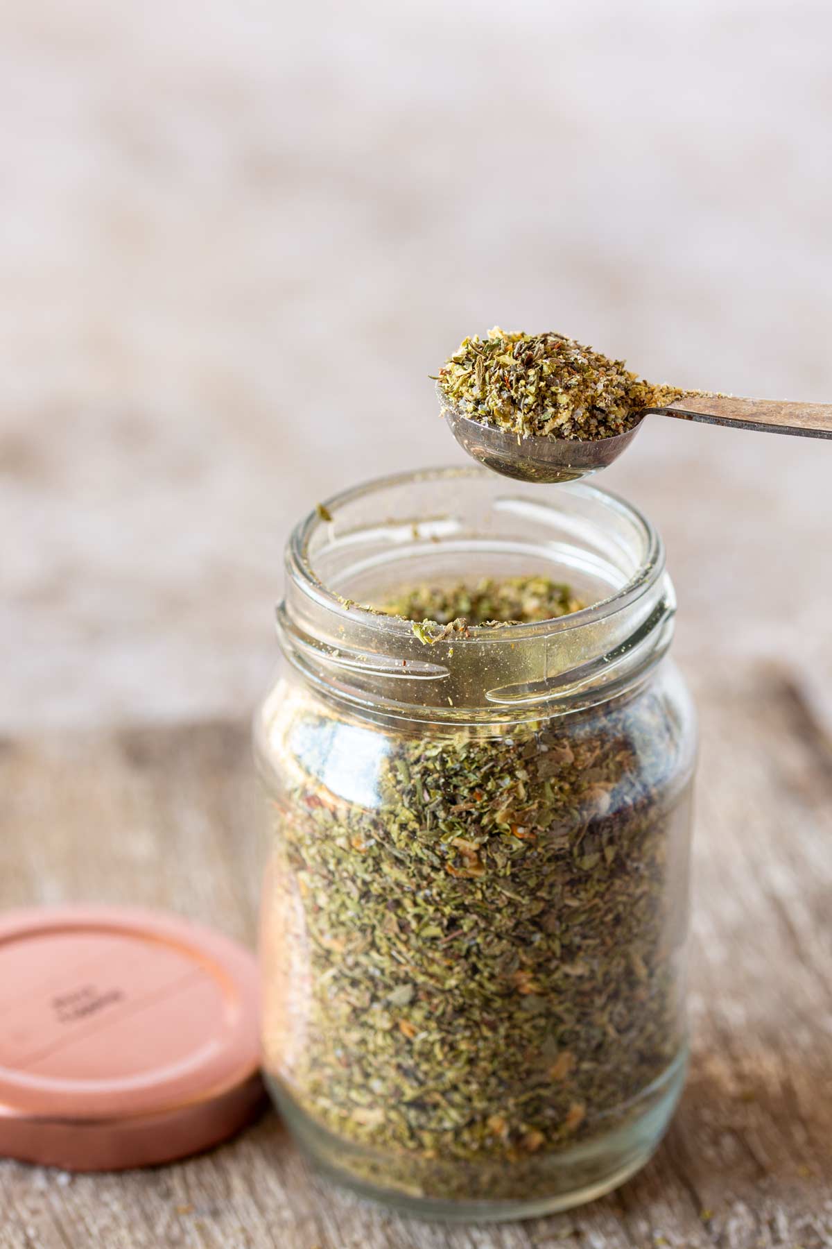 a measuring spoon lifting pizza seasoning from a glass jar