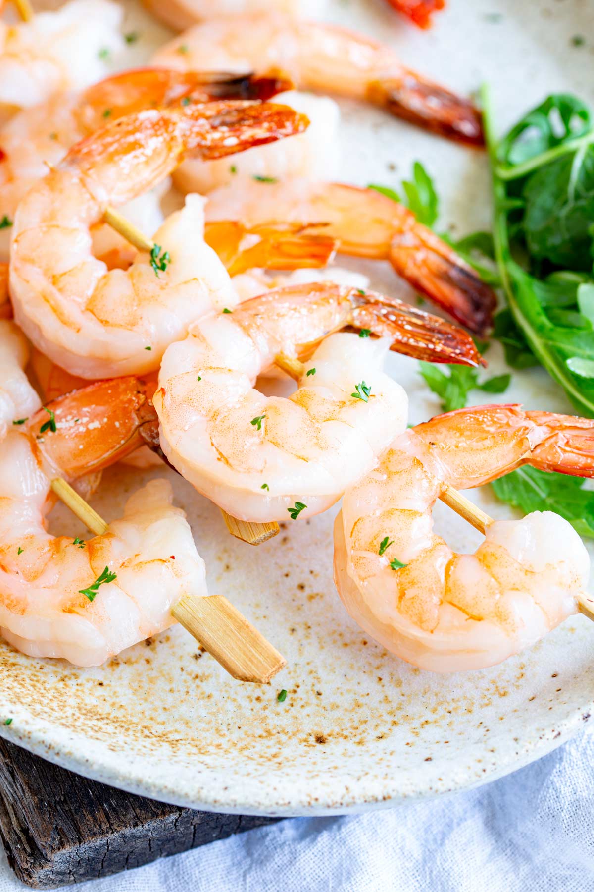 Shrimp skewers with three shrimp each, on a cream-colored plate with chopped parsley and green salad on the side
